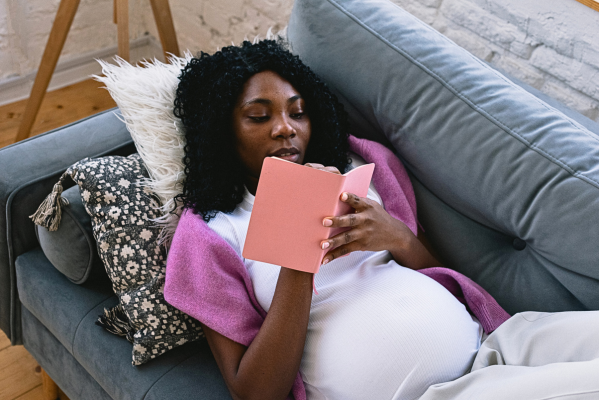 Black pregnant woman sitting on a couch, writing in a notebook while researching IVF success rate.
