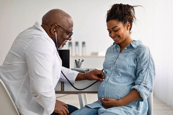 A Male experienced doctor examining a young pregnant woman during a consultation, highlighting the connection between pregnancy and mental health.